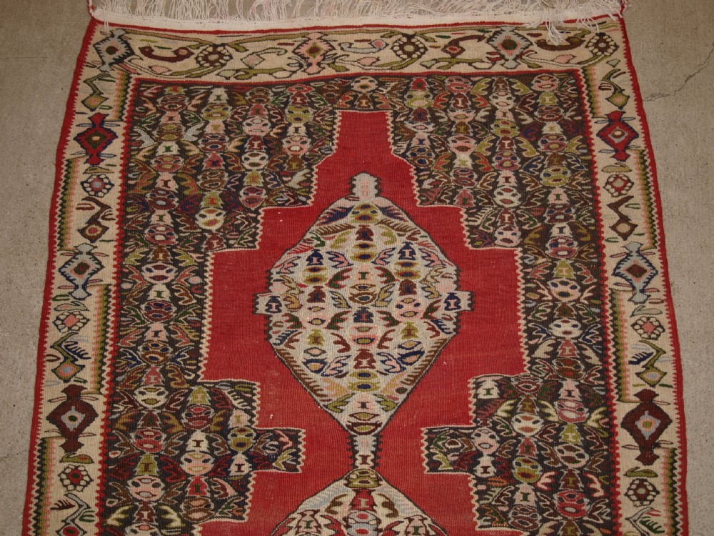 An antique Persian Senneh kilim runner featuring a sequence of linked diamond medallions on a vibrant red field with intricate geometric borders. View III