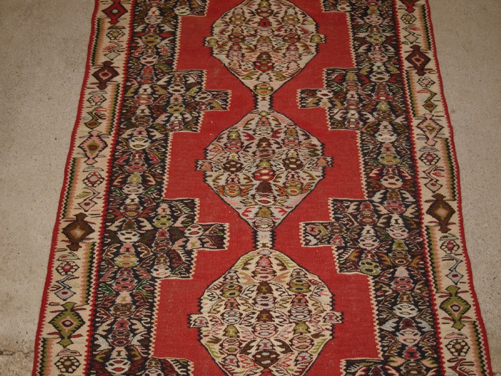 An antique Persian Senneh kilim runner featuring a sequence of linked diamond medallions on a vibrant red field with intricate geometric borders. View IV