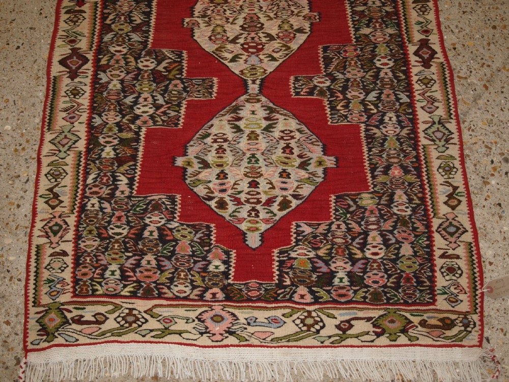 An antique Persian Senneh kilim runner featuring a sequence of linked diamond medallions on a vibrant red field with intricate geometric borders. View VI