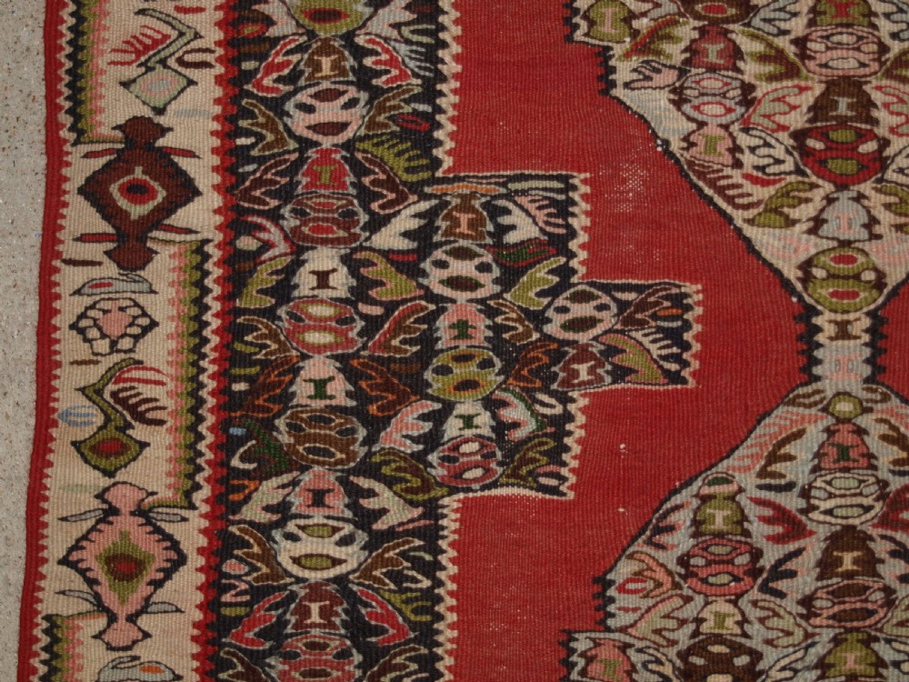An antique Persian Senneh kilim runner featuring a sequence of linked diamond medallions on a vibrant red field with intricate geometric borders. View IX
