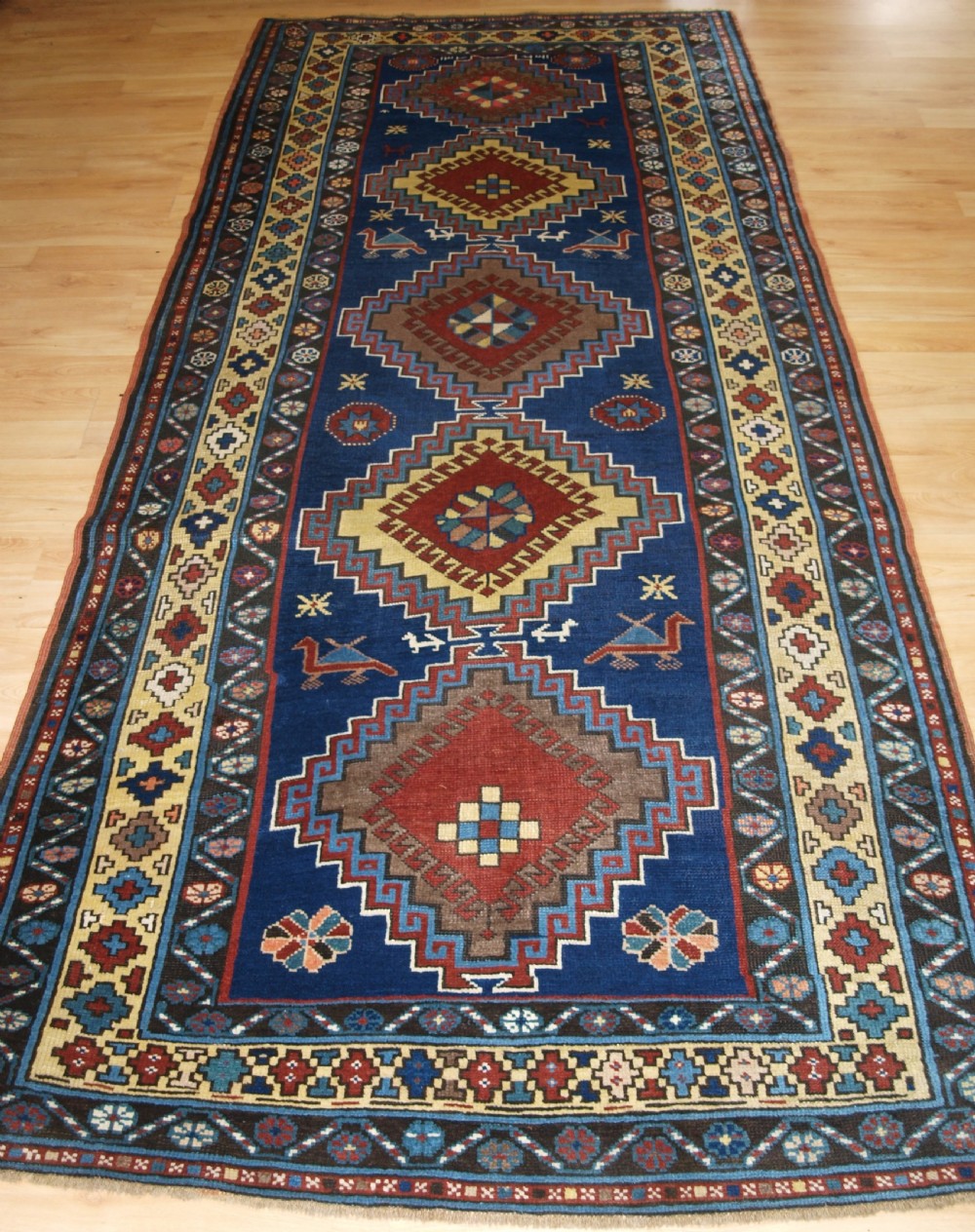 An antique Caucasian Kazak long rug featuring five stepped diamond medallions along a rich indigo blue field, framed by decorative geometric borders.