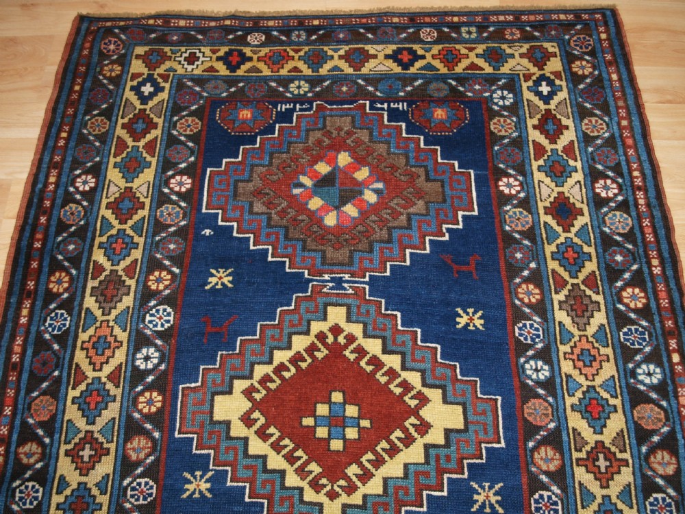 An antique Caucasian Kazak long rug featuring five stepped diamond medallions along a rich indigo blue field, framed by decorative geometric borders. View IV