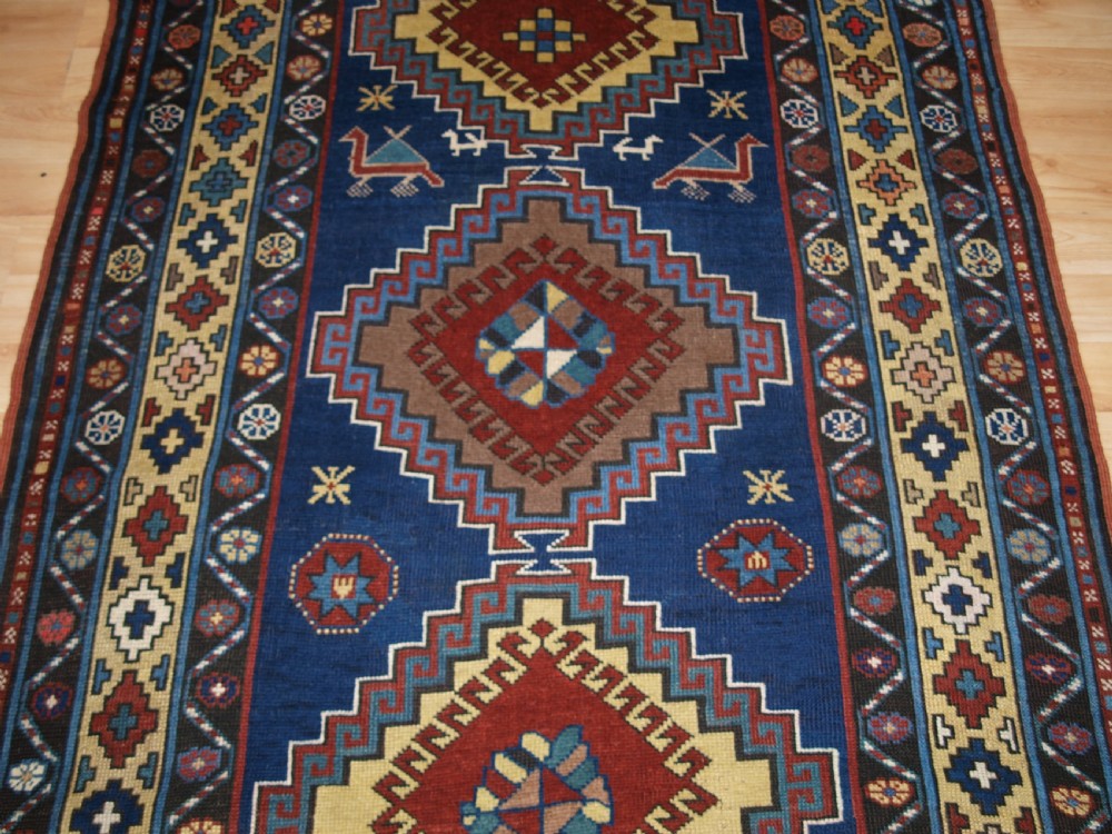 An antique Caucasian Kazak long rug featuring five stepped diamond medallions along a rich indigo blue field, framed by decorative geometric borders. View V