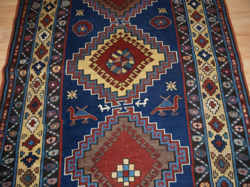 An antique Caucasian Kazak long rug featuring five stepped diamond medallions along a rich indigo blue field, framed by decorative geometric borders. View VI