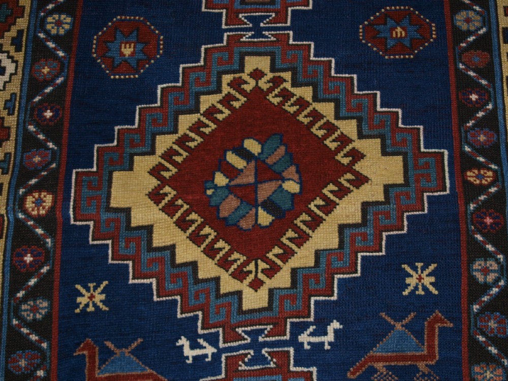 An antique Caucasian Kazak long rug featuring five stepped diamond medallions along a rich indigo blue field, framed by decorative geometric borders. View X