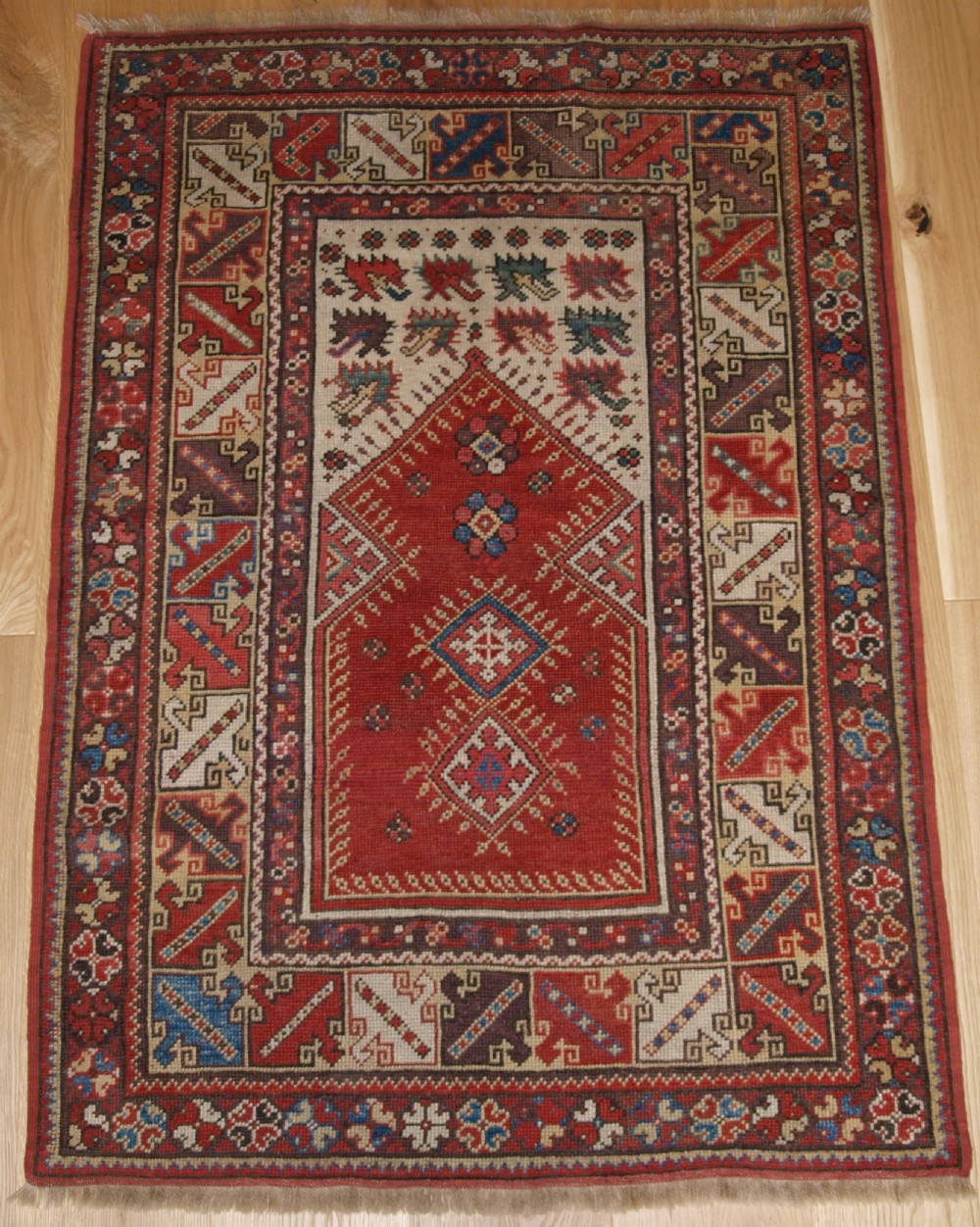 A late 19th-century Anatolian wool rug featuring a terracotta red geometric stepped mihrab niche framed by patterned multi-tiered borders in cream, blue, and red.