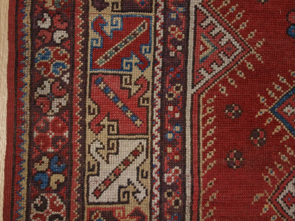 A late 19th-century Anatolian wool rug featuring a terracotta red geometric stepped mihrab niche framed by patterned multi-tiered borders in cream, blue, and red. View III