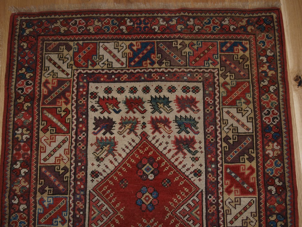 A late 19th-century Anatolian wool rug featuring a terracotta red geometric stepped mihrab niche framed by patterned multi-tiered borders in cream, blue, and red. View IV