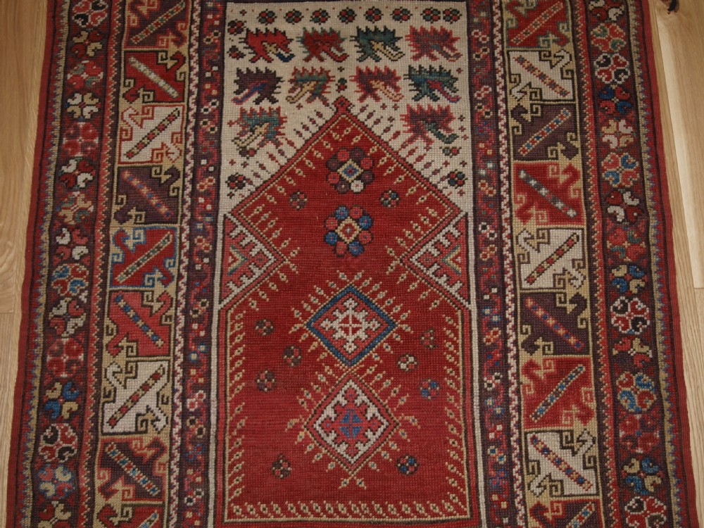 A late 19th-century Anatolian wool rug featuring a terracotta red geometric stepped mihrab niche framed by patterned multi-tiered borders in cream, blue, and red. View V