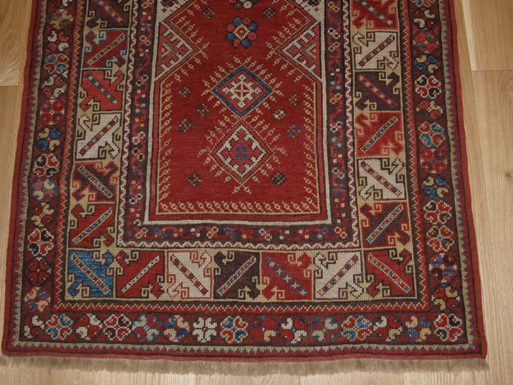 A late 19th-century Anatolian wool rug featuring a terracotta red geometric stepped mihrab niche framed by patterned multi-tiered borders in cream, blue, and red. View VI