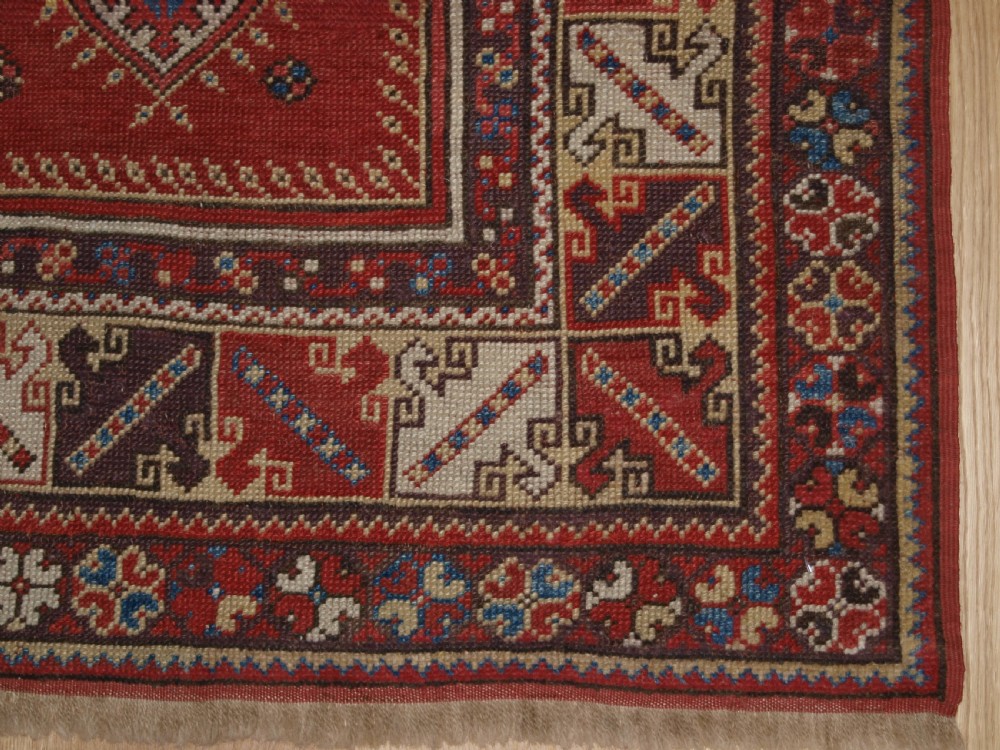 A late 19th-century Anatolian wool rug featuring a terracotta red geometric stepped mihrab niche framed by patterned multi-tiered borders in cream, blue, and red. View X