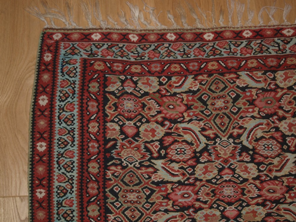 An antique flatwoven Persian Senneh kilim rug featuring a detailed central rectangle and surrounding border filled with intricate geometric and floral Herati patterns in red, ivory, and dark tones. View III