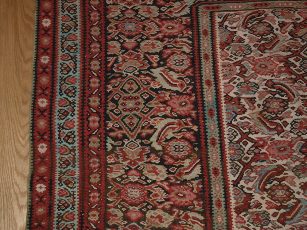 An antique flatwoven Persian Senneh kilim rug featuring a detailed central rectangle and surrounding border filled with intricate geometric and floral Herati patterns in red, ivory, and dark tones. View IV