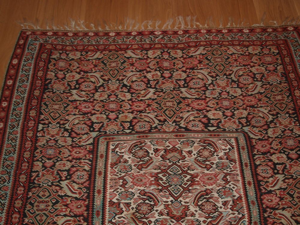 An antique flatwoven Persian Senneh kilim rug featuring a detailed central rectangle and surrounding border filled with intricate geometric and floral Herati patterns in red, ivory, and dark tones. View VI
