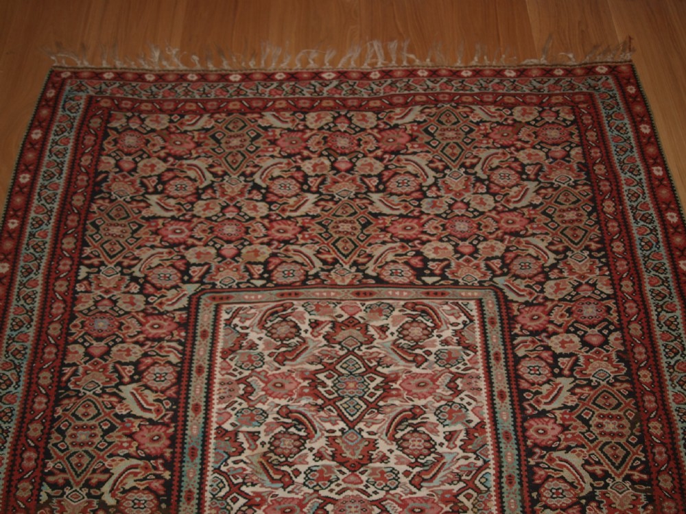 An antique flatwoven Persian Senneh kilim rug featuring a detailed central rectangle and surrounding border filled with intricate geometric and floral Herati patterns in red, ivory, and dark tones. View VII