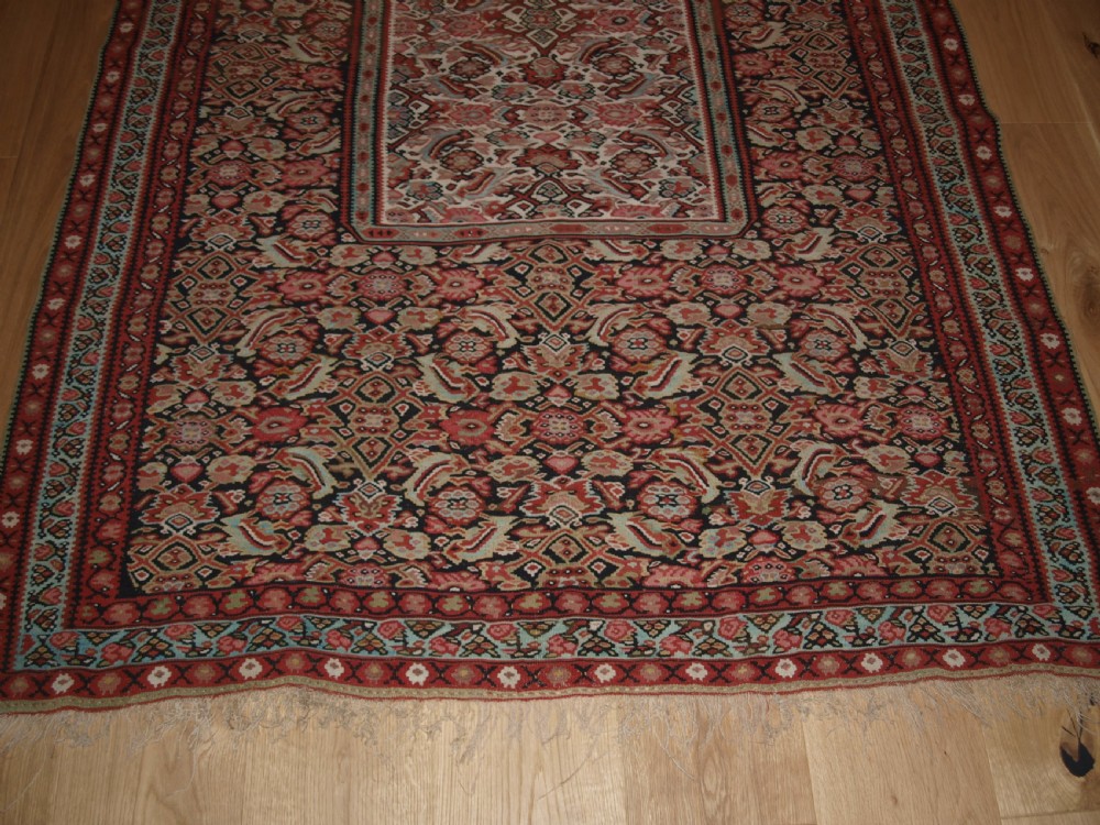 An antique flatwoven Persian Senneh kilim rug featuring a detailed central rectangle and surrounding border filled with intricate geometric and floral Herati patterns in red, ivory, and dark tones. View IX