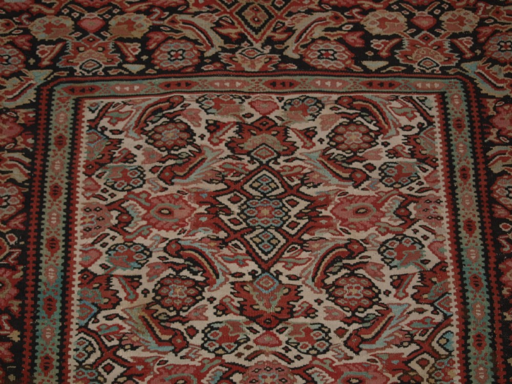 An antique flatwoven Persian Senneh kilim rug featuring a detailed central rectangle and surrounding border filled with intricate geometric and floral Herati patterns in red, ivory, and dark tones. View X
