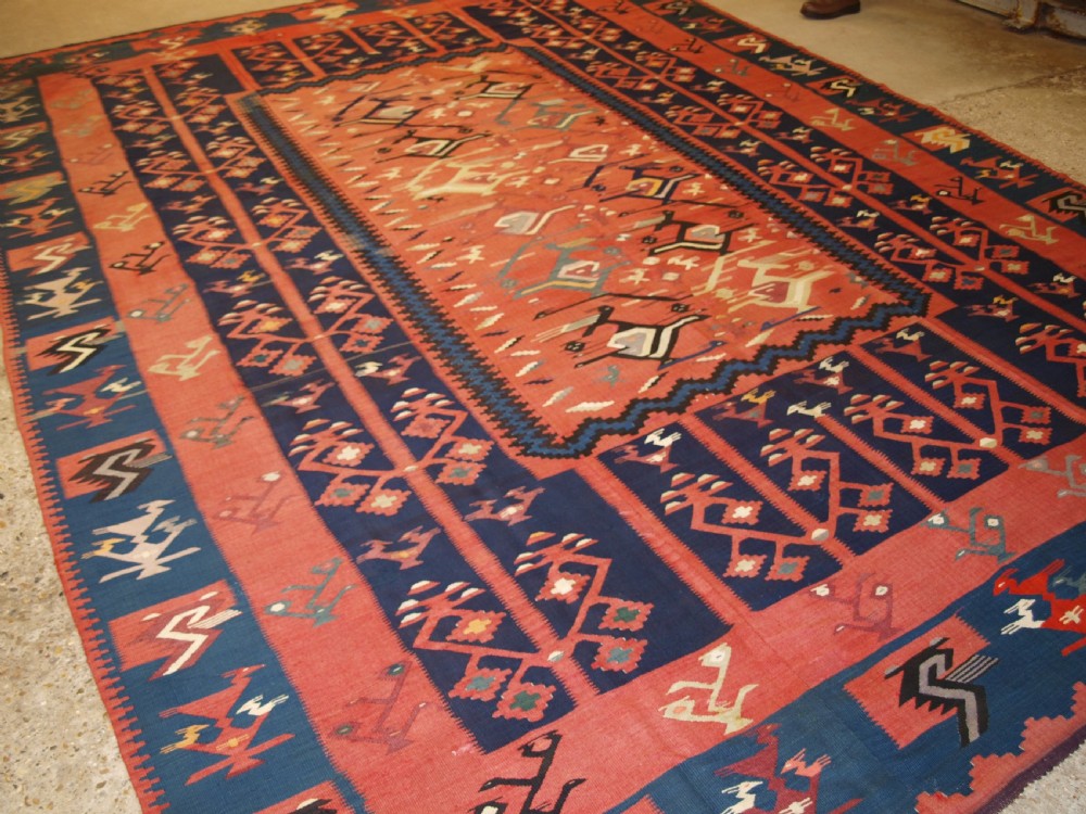 A large flatwoven Balkan Sharkoy kilim rug featuring terracotta red and navy blue borders decorated with stylised bird motifs and geometric patterns.