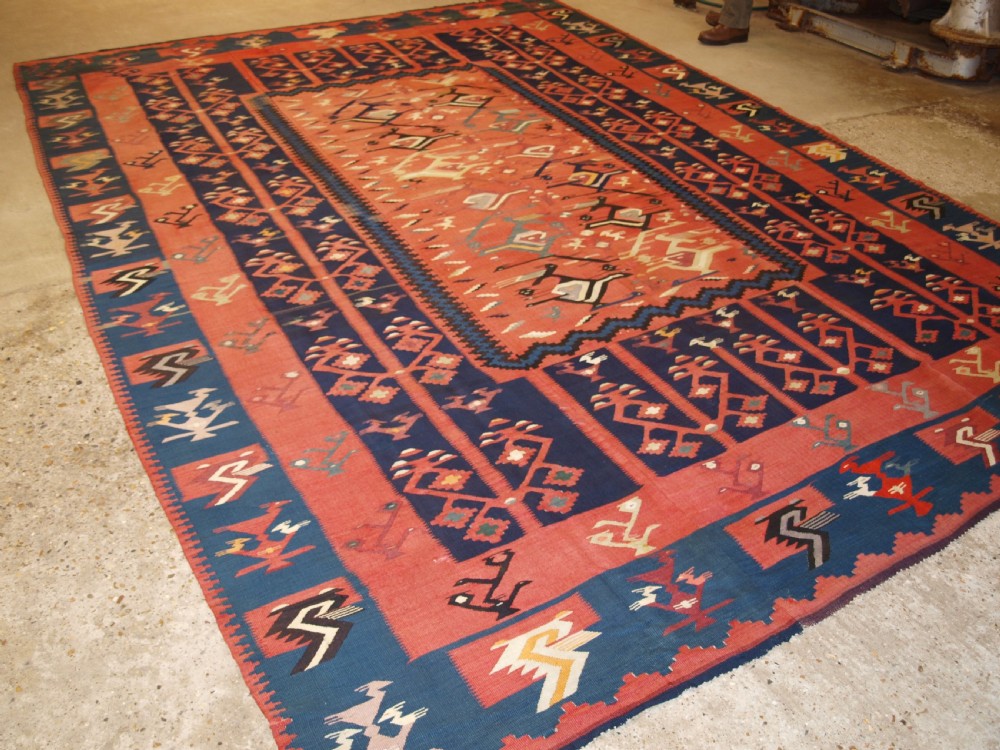 A large flatwoven Balkan Sharkoy kilim rug featuring terracotta red and navy blue borders decorated with stylised bird motifs and geometric patterns. View II