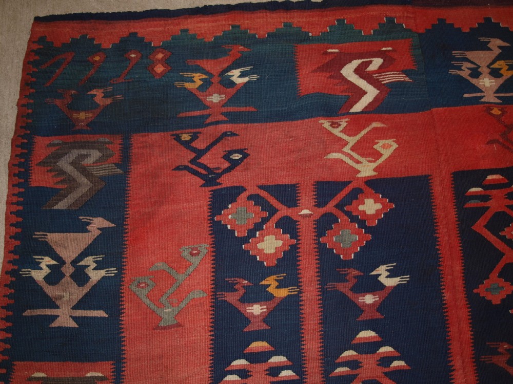 A large flatwoven Balkan Sharkoy kilim rug featuring terracotta red and navy blue borders decorated with stylised bird motifs and geometric patterns. View III