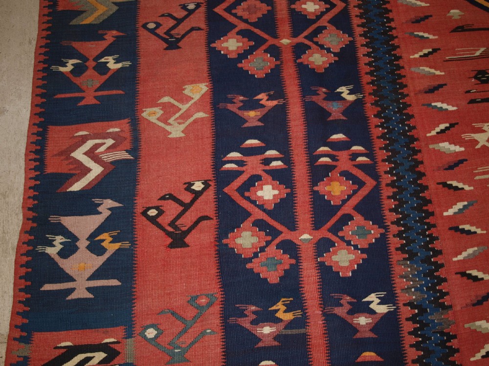 A large flatwoven Balkan Sharkoy kilim rug featuring terracotta red and navy blue borders decorated with stylised bird motifs and geometric patterns. View IV