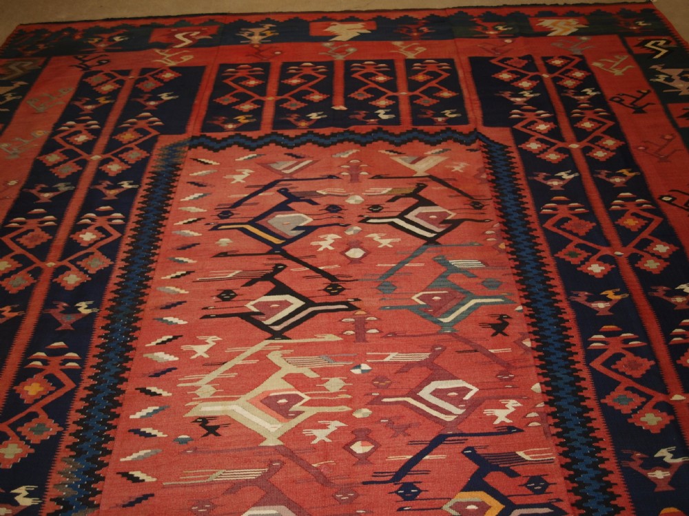 A large flatwoven Balkan Sharkoy kilim rug featuring terracotta red and navy blue borders decorated with stylised bird motifs and geometric patterns. View V