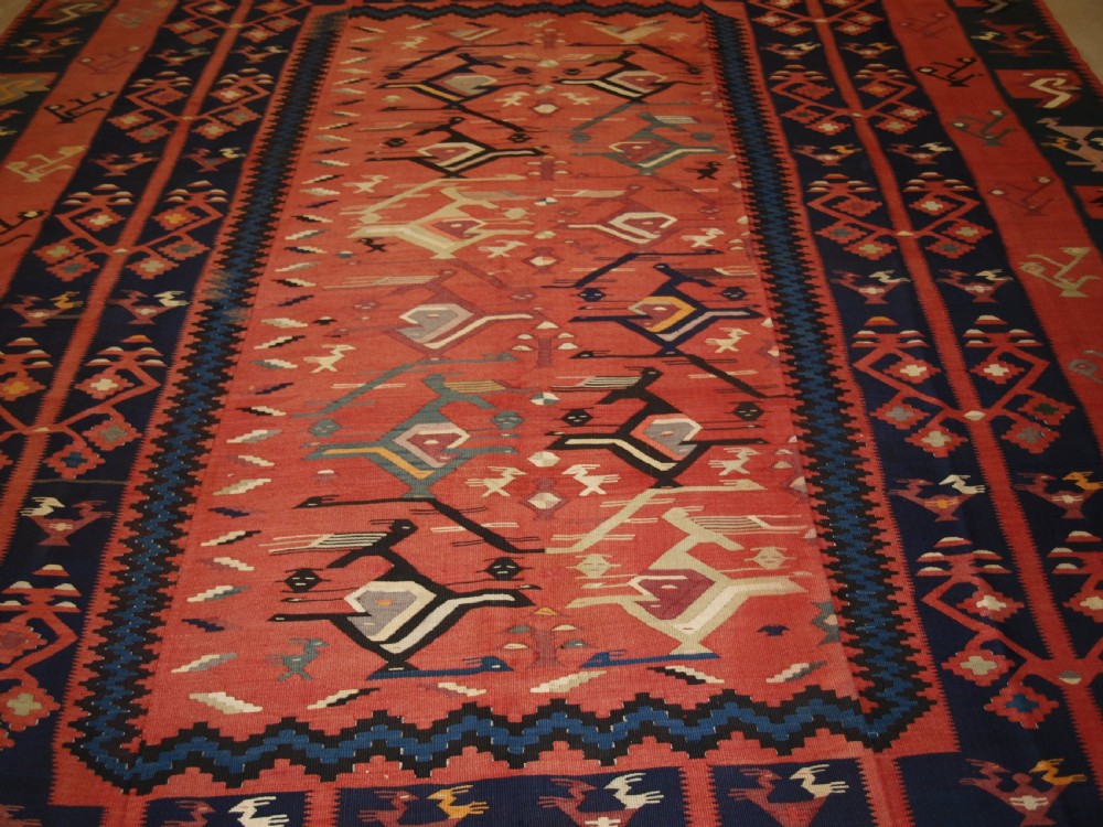 A large flatwoven Balkan Sharkoy kilim rug featuring terracotta red and navy blue borders decorated with stylised bird motifs and geometric patterns. View VI
