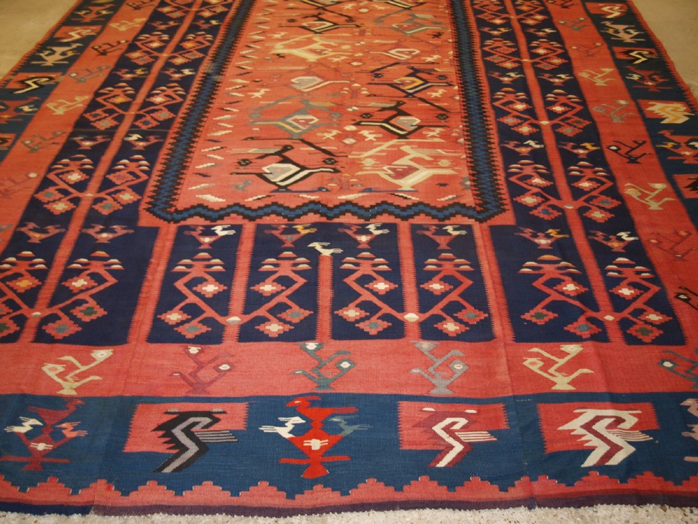 A large flatwoven Balkan Sharkoy kilim rug featuring terracotta red and navy blue borders decorated with stylised bird motifs and geometric patterns. View VII
