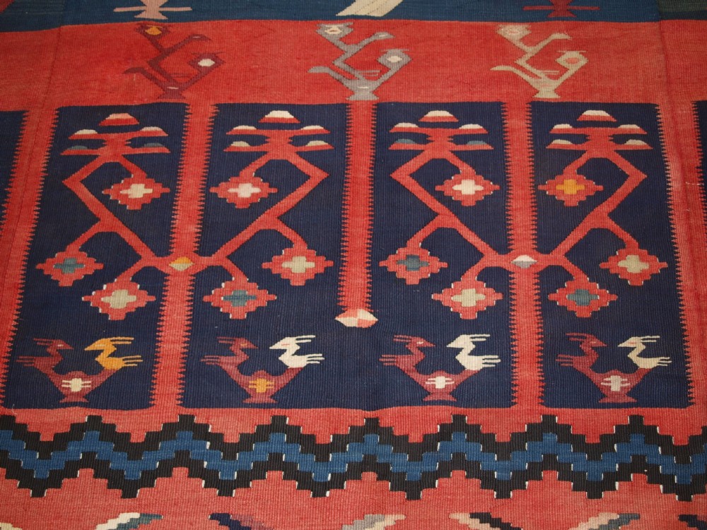 A large flatwoven Balkan Sharkoy kilim rug featuring terracotta red and navy blue borders decorated with stylised bird motifs and geometric patterns. View X