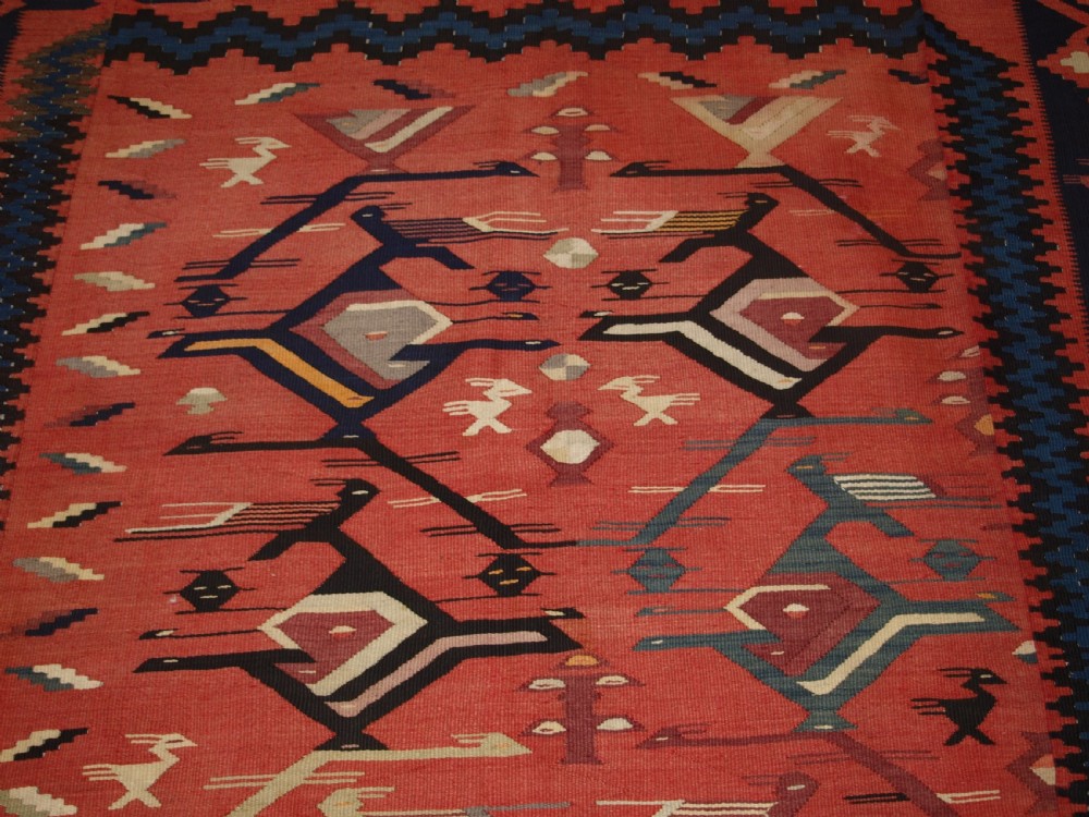 A large flatwoven Balkan Sharkoy kilim rug featuring terracotta red and navy blue borders decorated with stylised bird motifs and geometric patterns. View XI