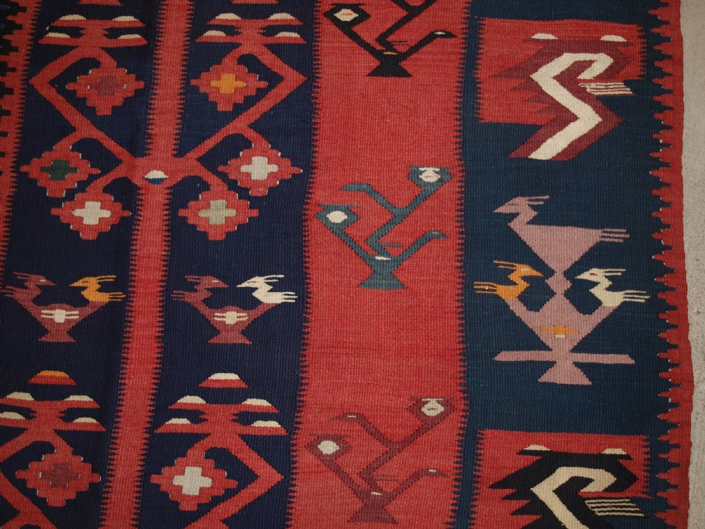 A large flatwoven Balkan Sharkoy kilim rug featuring terracotta red and navy blue borders decorated with stylised bird motifs and geometric patterns. View XIII