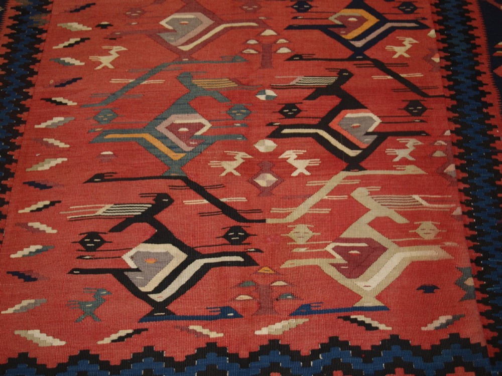 A large flatwoven Balkan Sharkoy kilim rug featuring terracotta red and navy blue borders decorated with stylised bird motifs and geometric patterns. View XIV