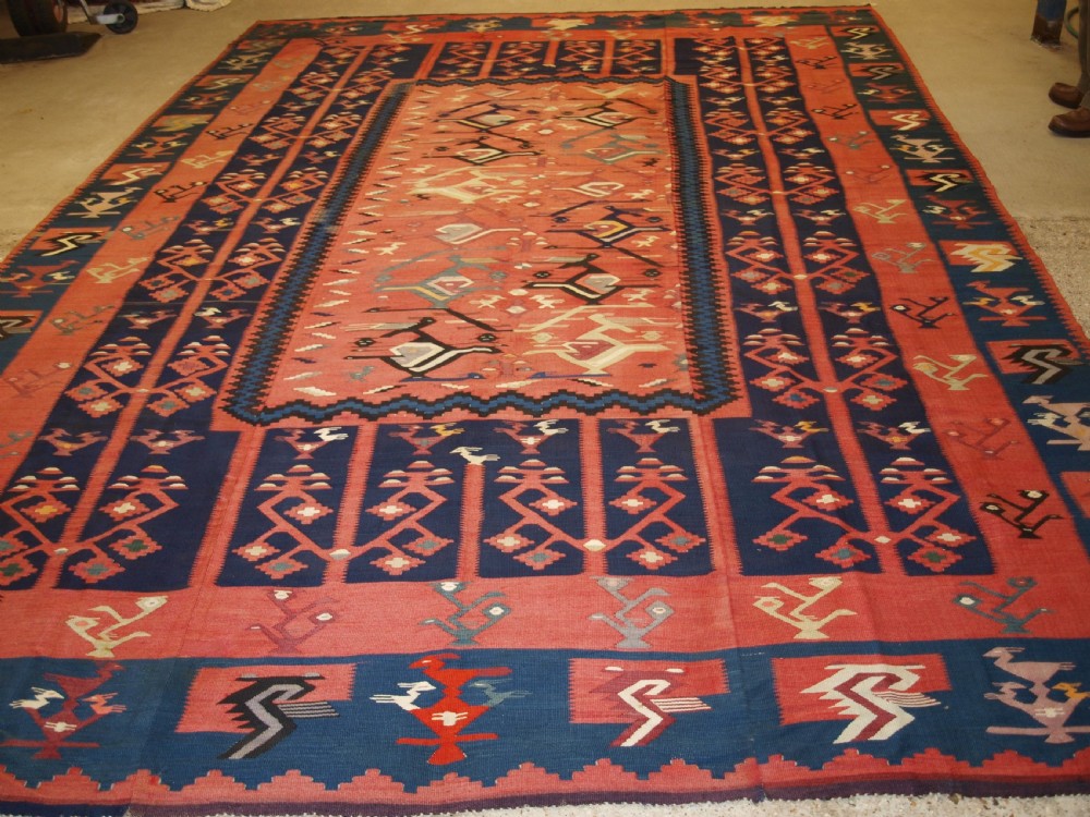 A large flatwoven Balkan Sharkoy kilim rug featuring terracotta red and navy blue borders decorated with stylised bird motifs and geometric patterns. View XVII
