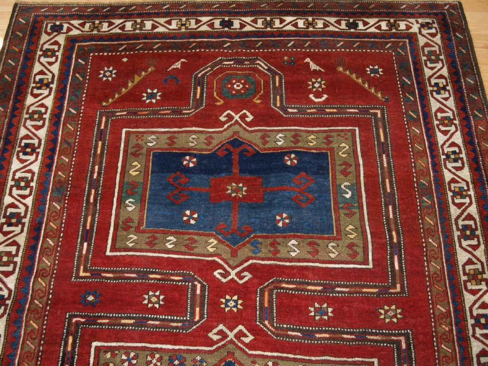 An antique Caucasian Fachralo Kazak hand-knotted wool long rug featuring a rich red field with three navy blue geometric medallions and elaborate borders. View II