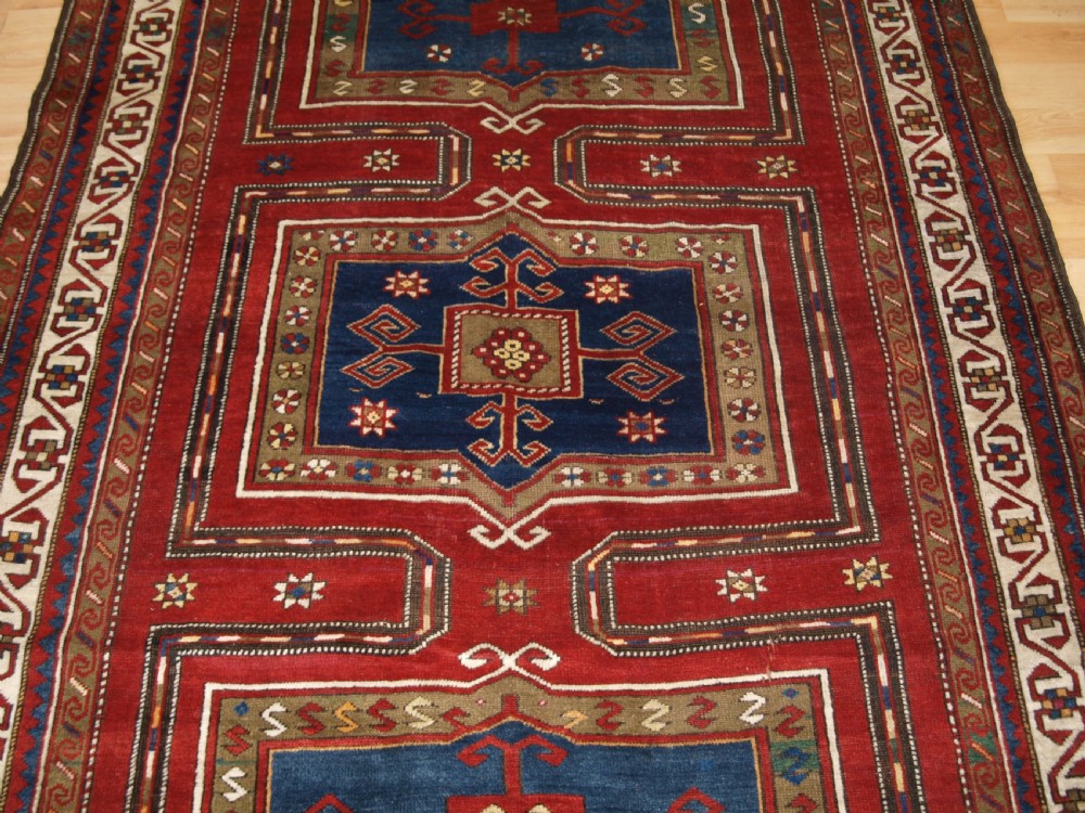 An antique Caucasian Fachralo Kazak hand-knotted wool long rug featuring a rich red field with three navy blue geometric medallions and elaborate borders. View III