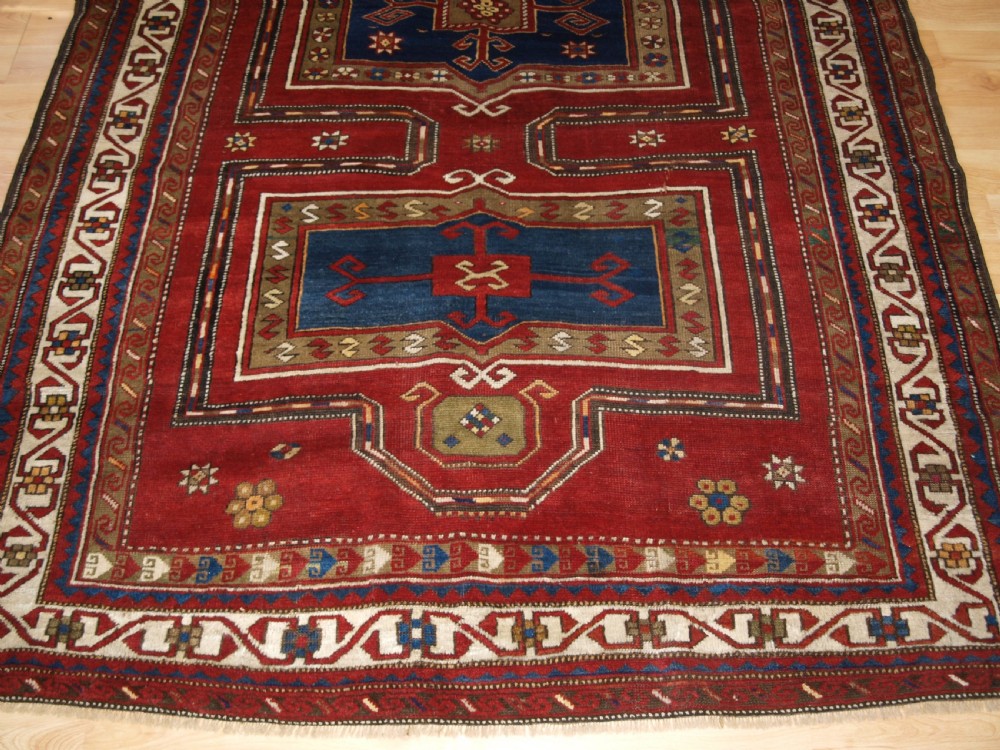 An antique Caucasian Fachralo Kazak hand-knotted wool long rug featuring a rich red field with three navy blue geometric medallions and elaborate borders. View IV