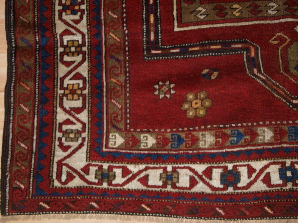 An antique Caucasian Fachralo Kazak hand-knotted wool long rug featuring a rich red field with three navy blue geometric medallions and elaborate borders. View V