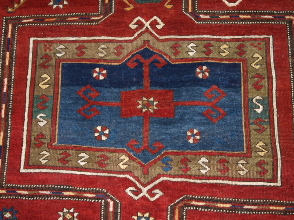An antique Caucasian Fachralo Kazak hand-knotted wool long rug featuring a rich red field with three navy blue geometric medallions and elaborate borders. View VI