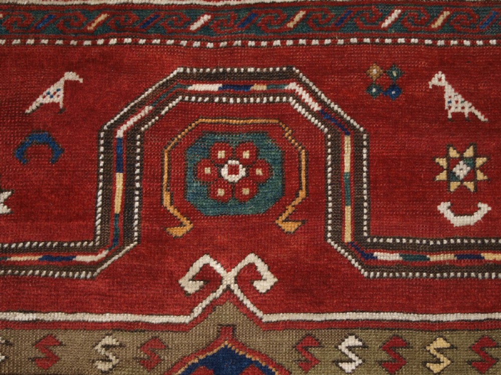 An antique Caucasian Fachralo Kazak hand-knotted wool long rug featuring a rich red field with three navy blue geometric medallions and elaborate borders. View VII
