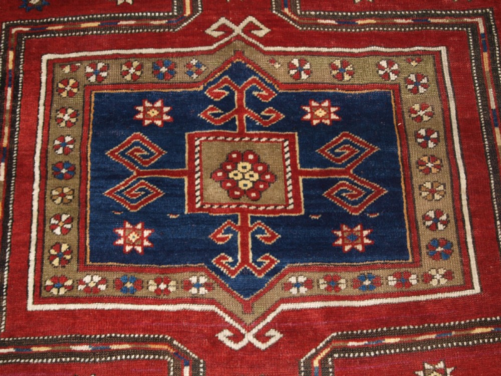 An antique Caucasian Fachralo Kazak hand-knotted wool long rug featuring a rich red field with three navy blue geometric medallions and elaborate borders. View VIII