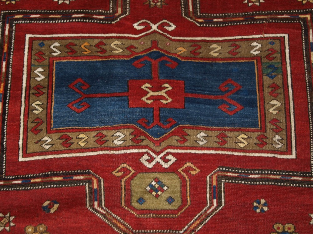 An antique Caucasian Fachralo Kazak hand-knotted wool long rug featuring a rich red field with three navy blue geometric medallions and elaborate borders. View IX