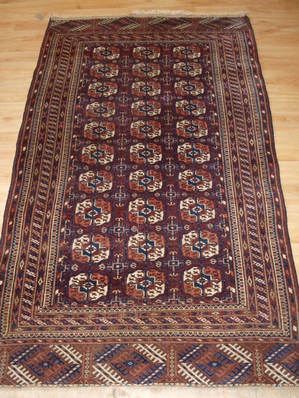 An antique Tekke Turkmen wool rug featuring repeating geometric gul motifs on a deep red ground with multi-layered patterned borders.