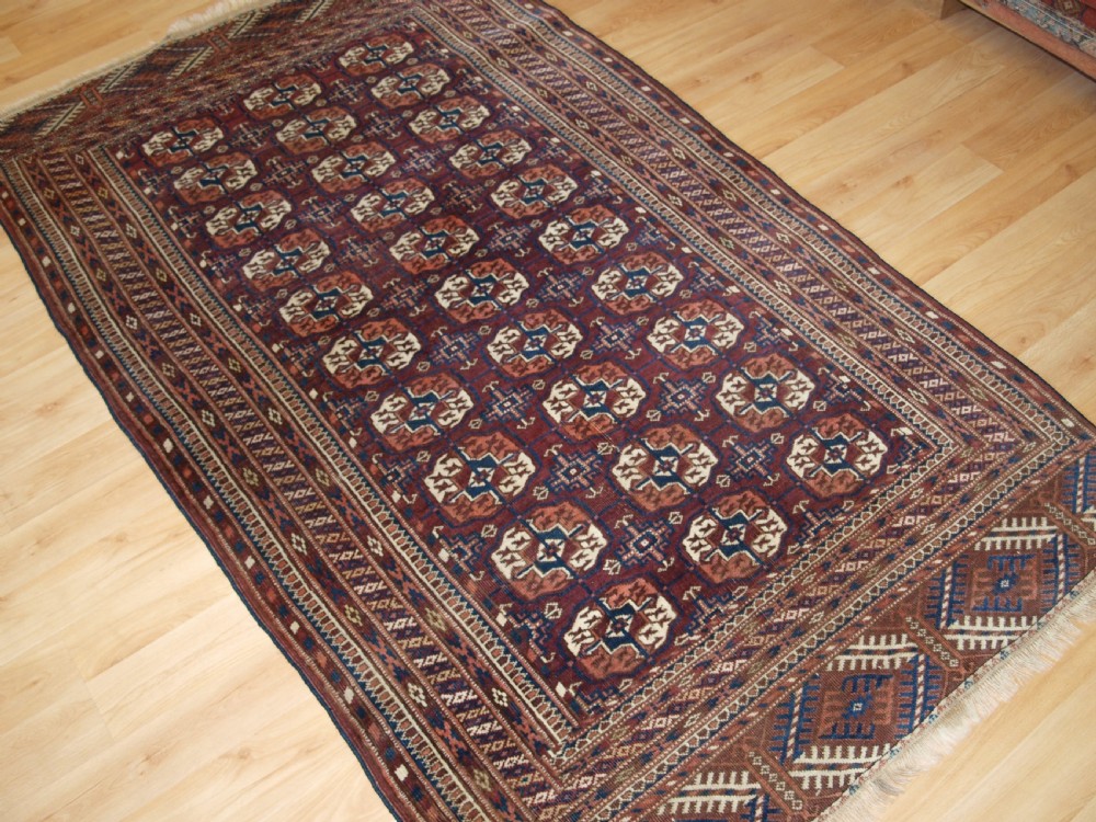 An antique Tekke Turkmen wool rug featuring repeating geometric gul motifs on a deep red ground with multi-layered patterned borders. View II