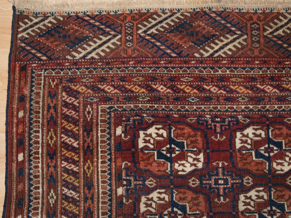 An antique Tekke Turkmen wool rug featuring repeating geometric gul motifs on a deep red ground with multi-layered patterned borders. View III