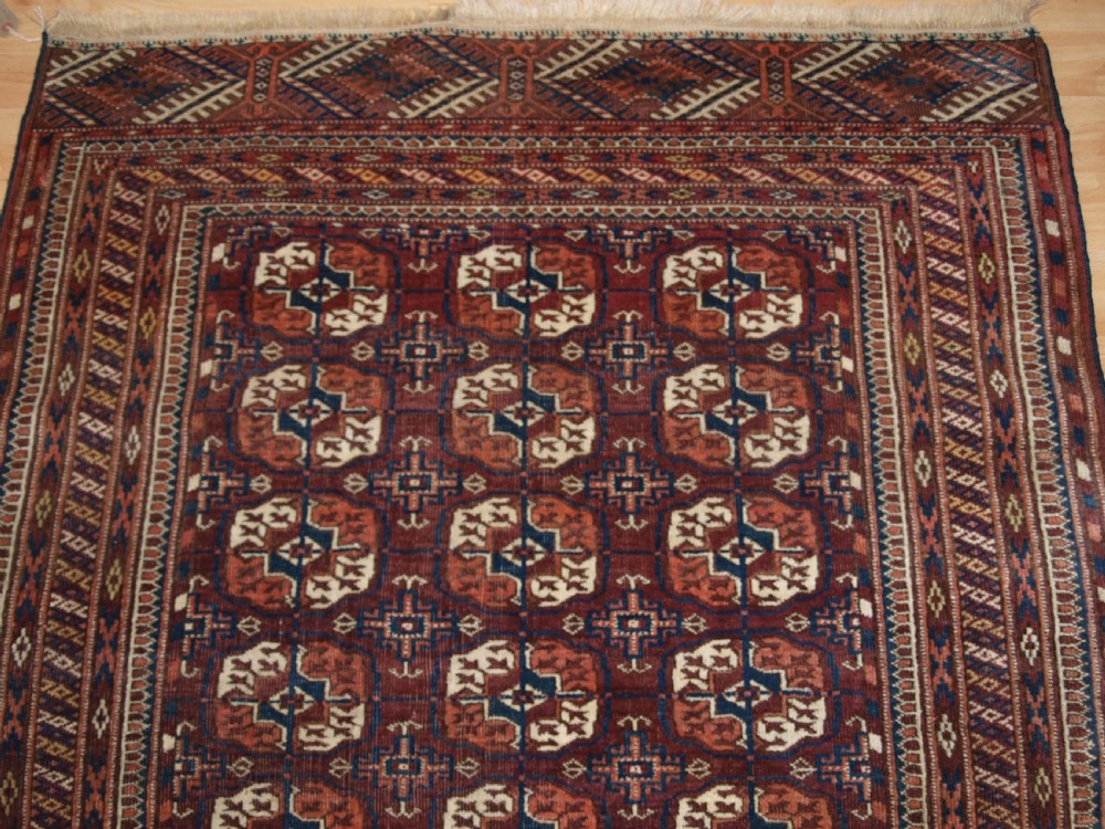 An antique Tekke Turkmen wool rug featuring repeating geometric gul motifs on a deep red ground with multi-layered patterned borders. View IV