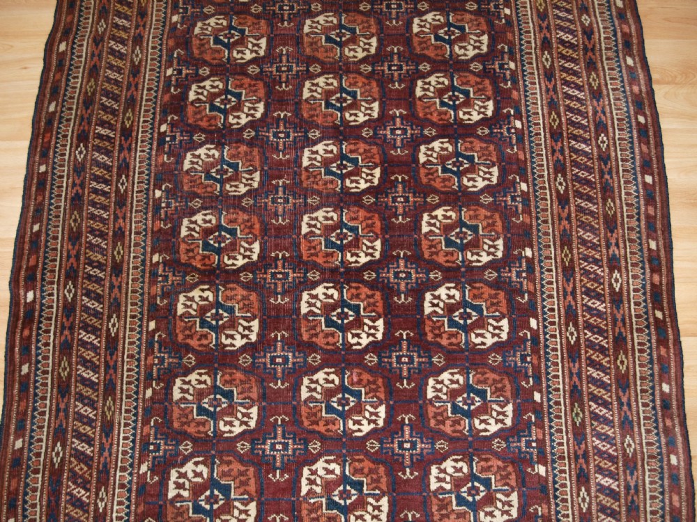 An antique Tekke Turkmen wool rug featuring repeating geometric gul motifs on a deep red ground with multi-layered patterned borders. View V