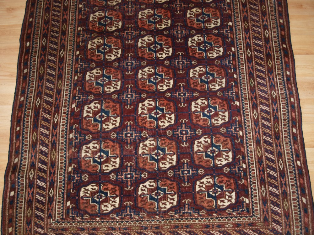 An antique Tekke Turkmen wool rug featuring repeating geometric gul motifs on a deep red ground with multi-layered patterned borders. View VI