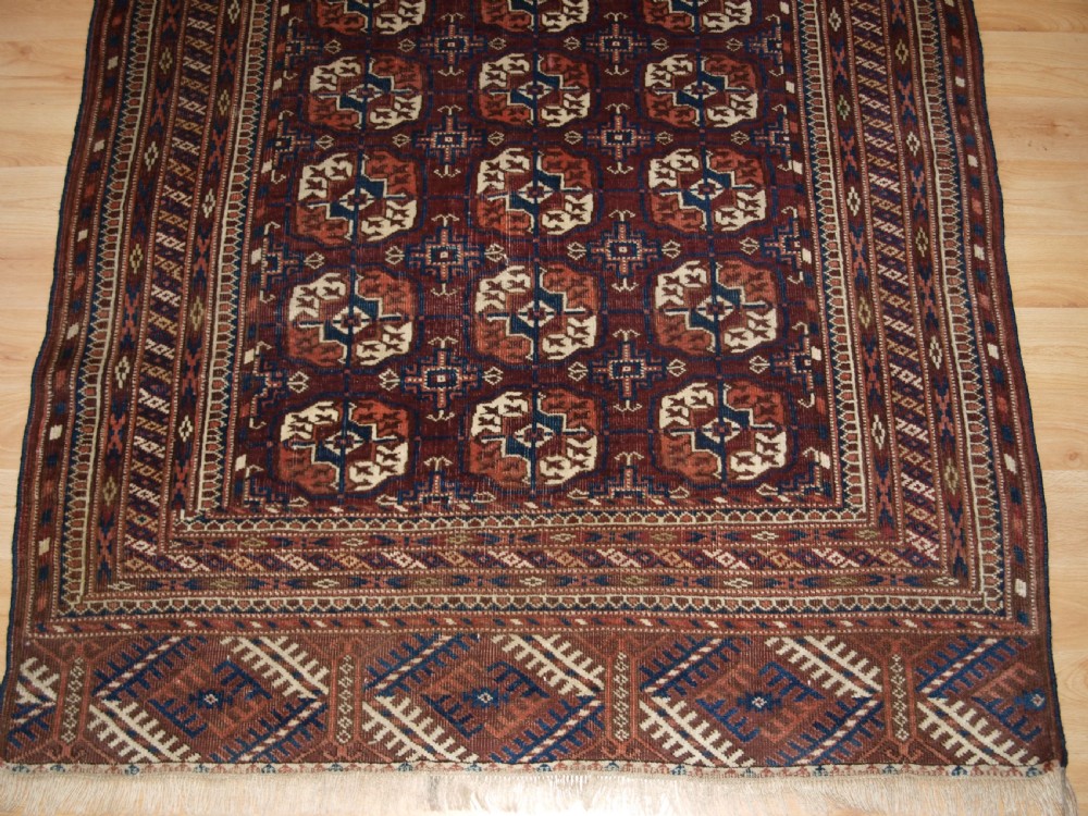 An antique Tekke Turkmen wool rug featuring repeating geometric gul motifs on a deep red ground with multi-layered patterned borders. View VII