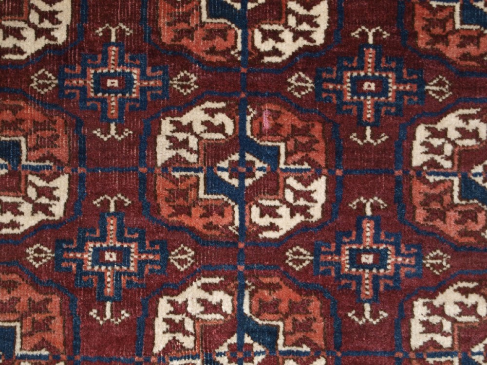 An antique Tekke Turkmen wool rug featuring repeating geometric gul motifs on a deep red ground with multi-layered patterned borders. View VIII