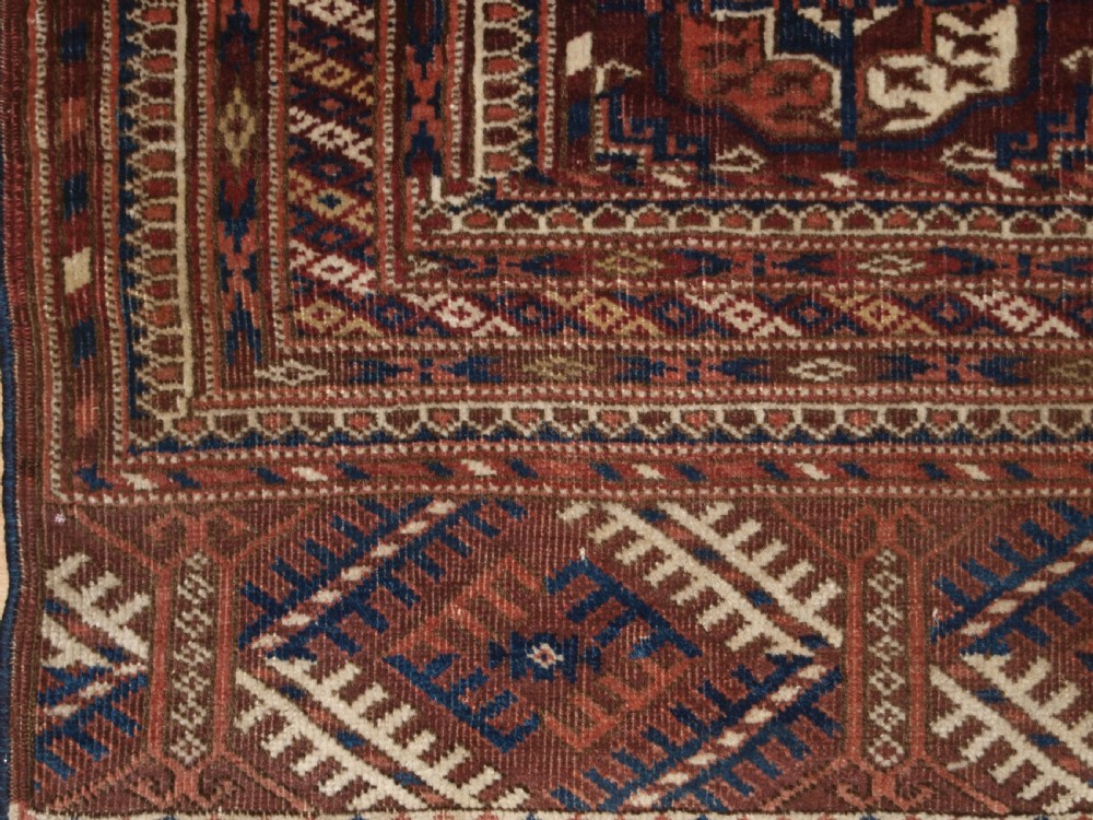An antique Tekke Turkmen wool rug featuring repeating geometric gul motifs on a deep red ground with multi-layered patterned borders. View IX